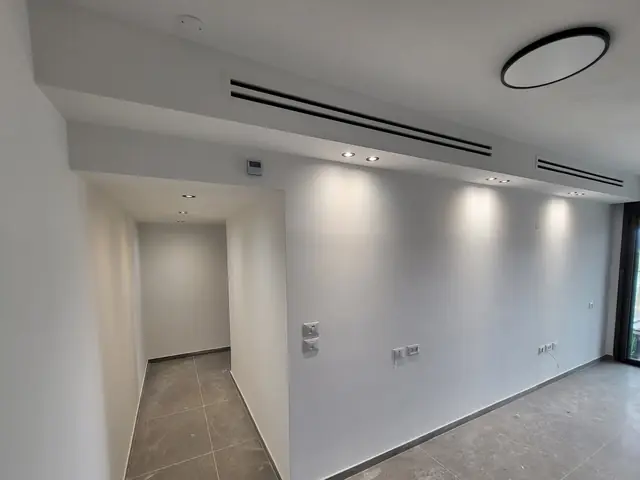 סלון לבן עם מפזרי מיזוג ליניאריים בתקרה של מערכת מיני מרכזי