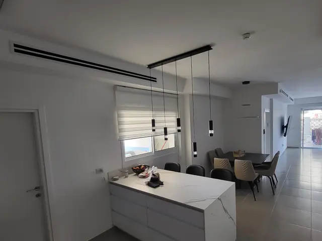 מטבח ופינת אוכל פתוחים עם פתחי מיזוג בתעלה שלאורך התקרה
