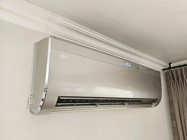 מזגן עילי כסוף מותקן על קיר בחדר, מתחת לכרכוב התקרה